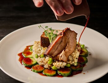 Pork belly over brown rice, cucumber, scallion, edamame. A composed plate that earns its restraint. The sauce arrives at the table still moving.